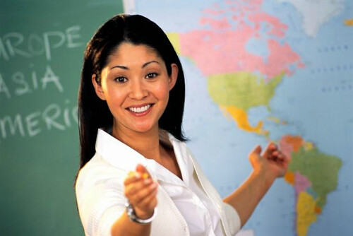 A picture of an Asian teacher in front of a world map and a chalkboard, sourced from the Creative Commons and user 'PTICA10.' Represents Project Three: Genre Translation Blog Post, March 2025-April 2025.